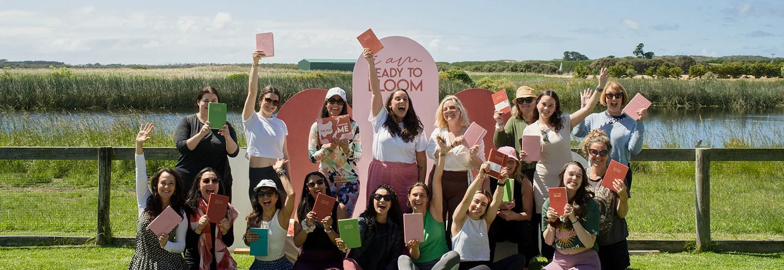 Veinte mujeres en un evento de I Am Ready To Bloom, al aire libre, cada una con su planner en la mano.